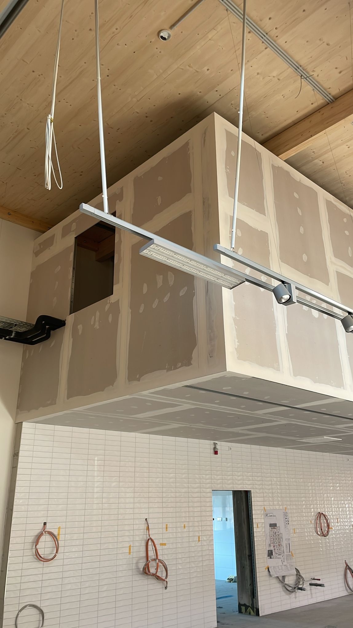 Wnętrze w trakcie wykańczania: ściany z płyt w systemie suchej zabudowy, widoczne łączenia płyt wymagające dalszej obróbki, podwieszany sufit, białe płytki na ścianie, instalacje elektryczne...