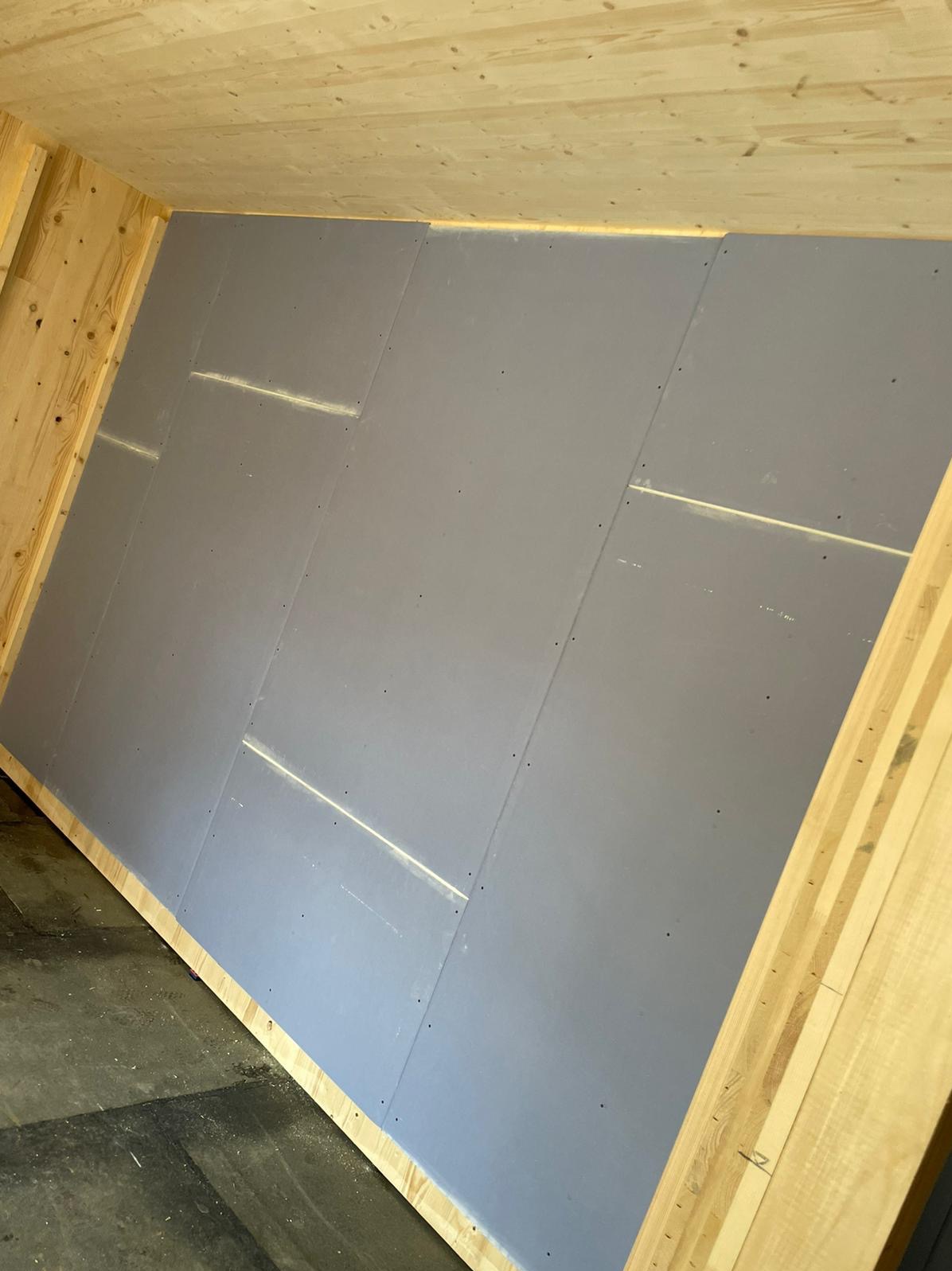 Skośna ściana poddasza z zamontowanymi szarymi płytami, widoczne drewniane elementy konstrukcyjne i łączenia płyt z widocznymi śladami szpachli.