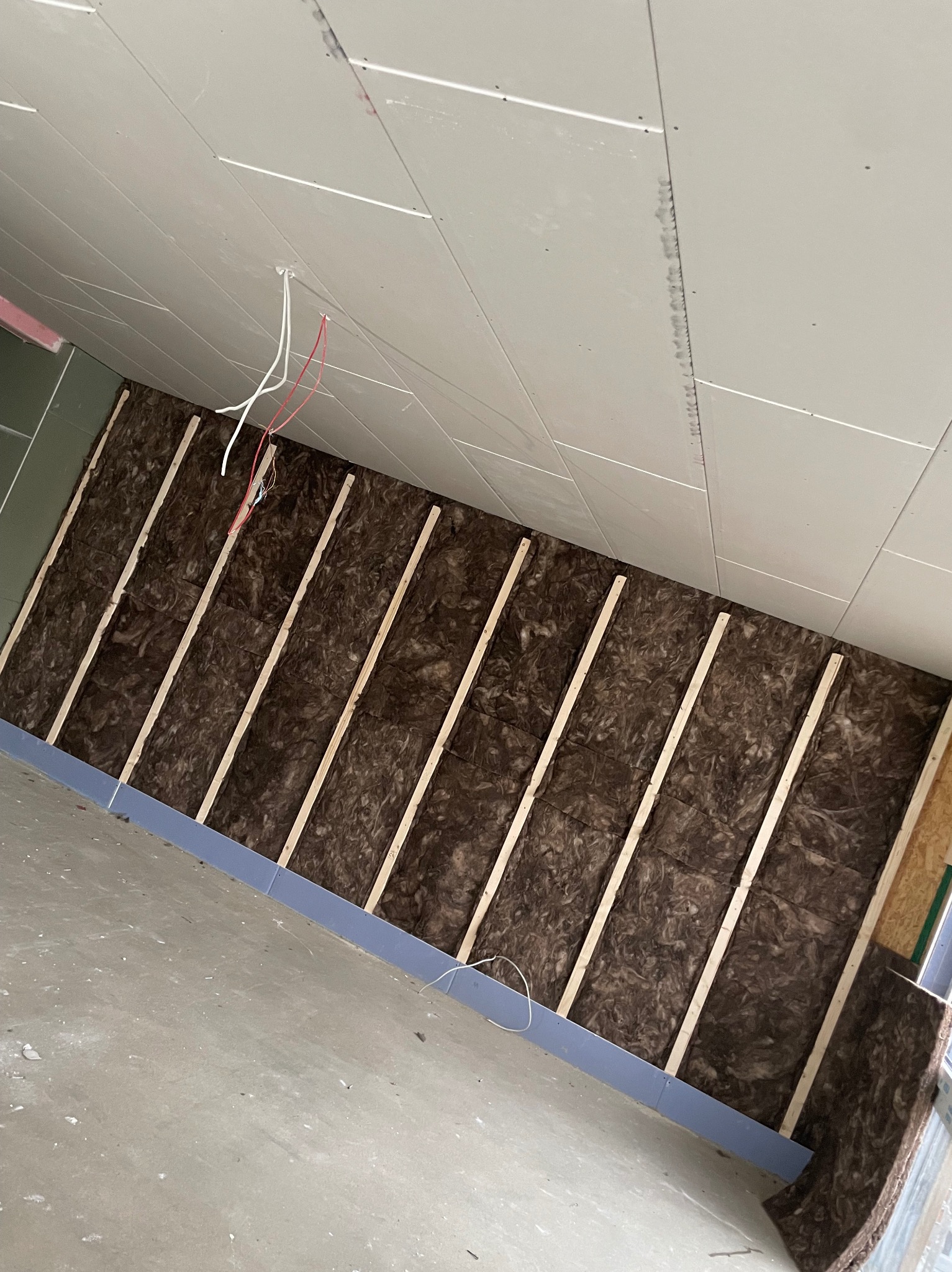 Wnętrze w trakcie prac wykończeniowych: ocieplone wełną mineralną poddasze z widoczną konstrukcją drewnianą i częściowo zamontowanymi płytami gipsowo-kartonowymi na suficie, zwisające przewody...