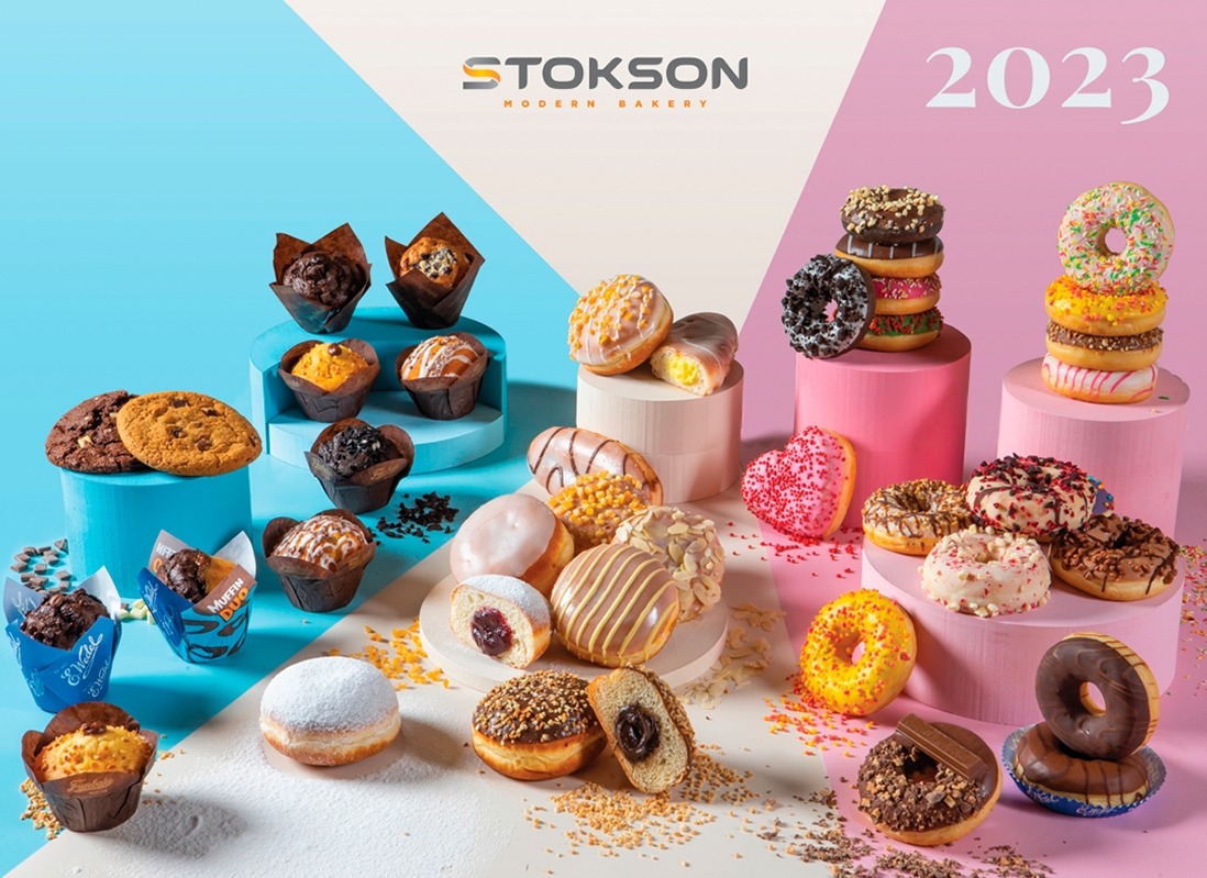 Apetyczna kompozycja wypieków z Rybnika: babeczki w papilotkach, ciasteczka i różnorodne pączki z polewami i posypkami, ułożone na podestach w pastelowych kolorach, z logo piekarni w tle i rokiem...