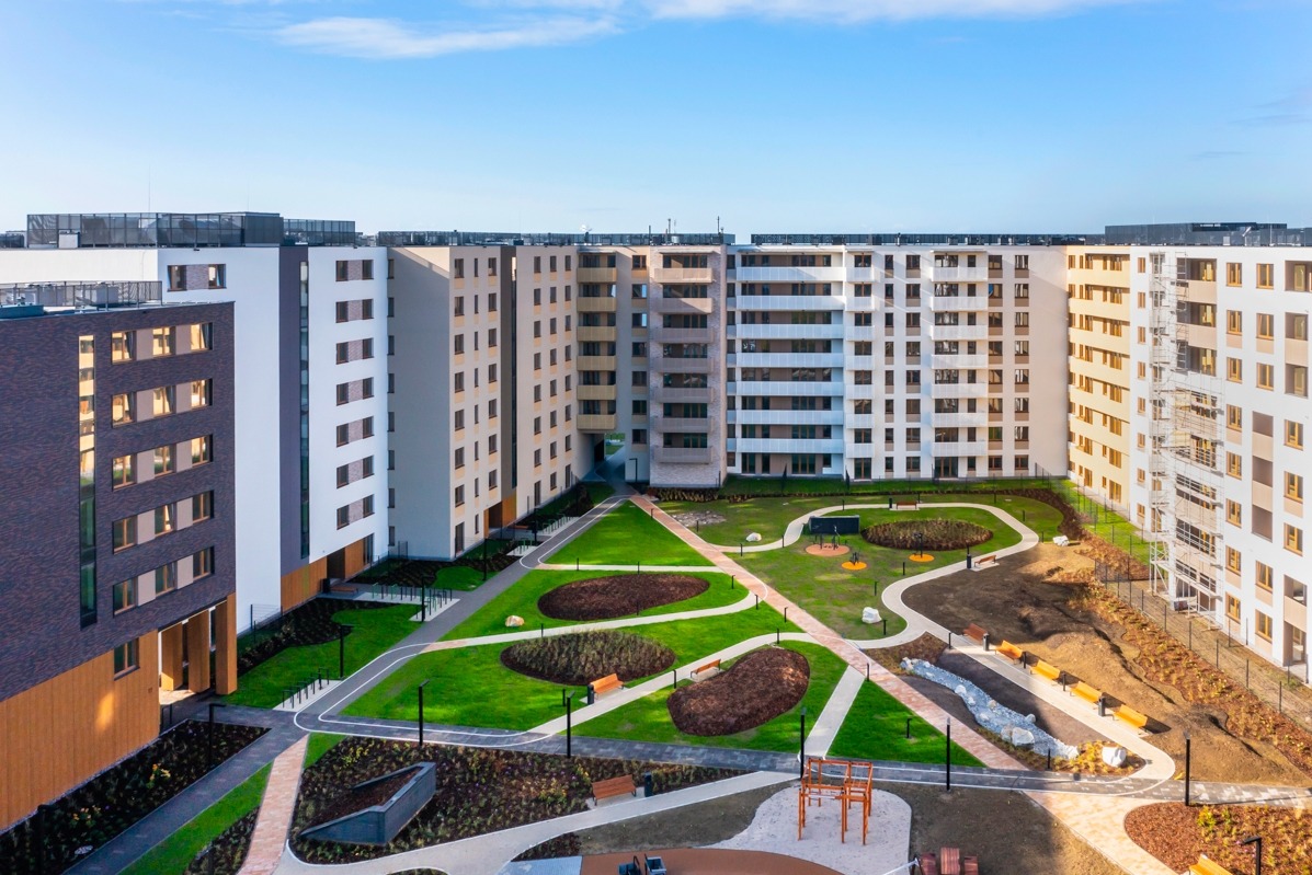 Widok z góry na nowo wybudowane osiedle mieszkaniowe z wewnętrznym dziedzińcem, gdzie znajdują się zielone trawniki, ścieżki, place zabaw i elementy małej architektury.