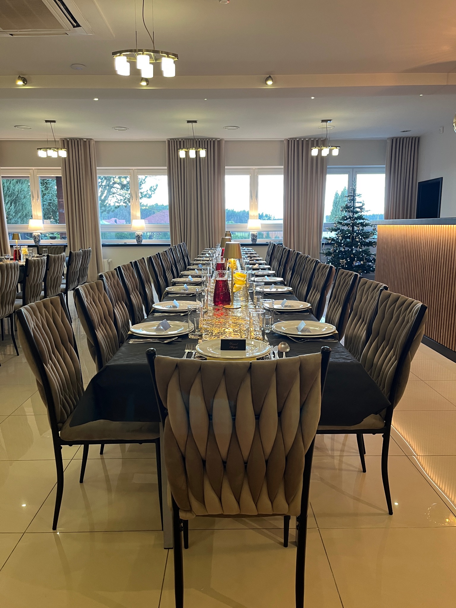 Uroczysta aranżacja stołu na przyjęcie z czarnym obrusem, elegancką zastawą, szklanymi naczyniami i dekoracjami, w tle widoczna choinka.