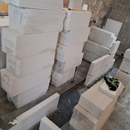 BUDRAF - Budowa ściany z białych bloczków betonu komórkowego, widoczne narzędzia murarskie, poziomica i sznurek traserski, surowe ściany w tle.