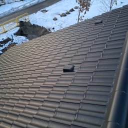 BUDRAF - Ukośny widok na nowy, grafitowy dach z ceramicznej dachówki falistej, z widocznym kominkiem wentylacyjnym i fragmentem rynny, na tle ośnieżonego otoczenia.