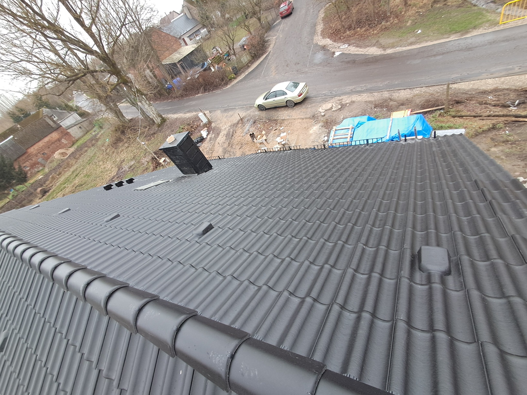 Nowy, ciemnoszary dach z dachówki ceramicznej, widok z góry na ukończony fragment, w tle zabudowania i ulica z samochodami.