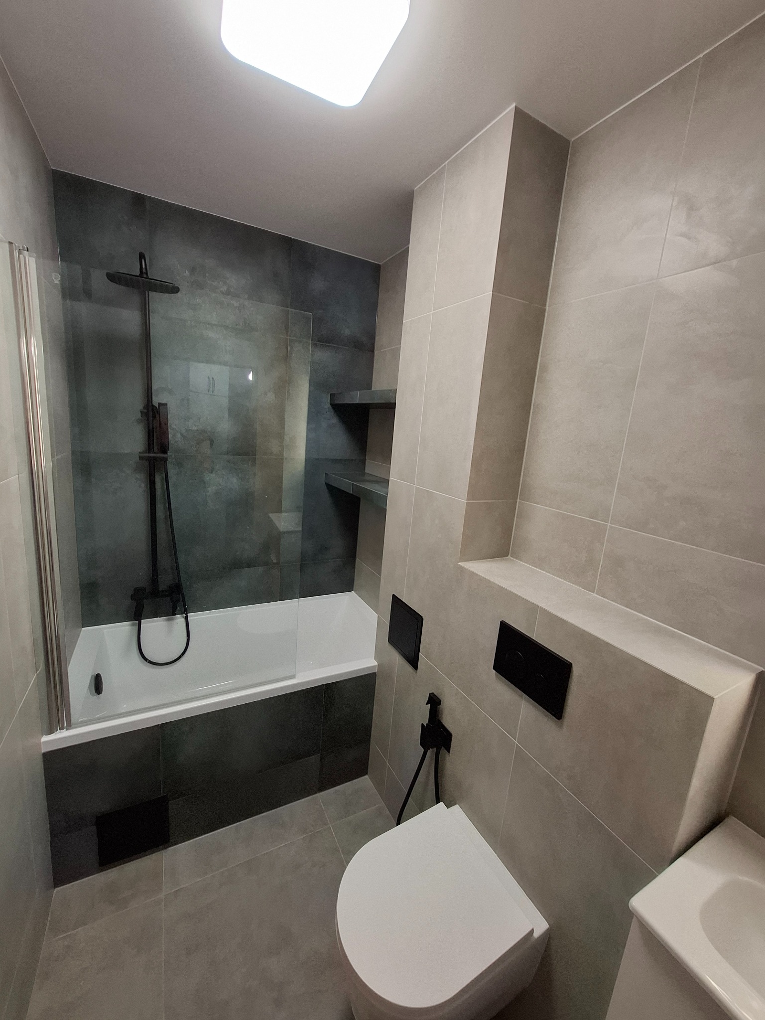 Nowoczesna łazienka z szarymi płytkami, czarną armaturą i kabiną prysznicową. Minimalistyczny design z podświetleniem i geometrycznymi akcentami.