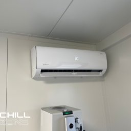 Chill Zone Mateusz Tomaszczuk - Biała klimatyzacja Rotenso z wyświetlaczem wskazującym 30 stopni, zamontowana na jasnej ścianie w pomieszczeniu z widocznym ekspresem do kawy Jura, w tle widoczne panele sufitowe.