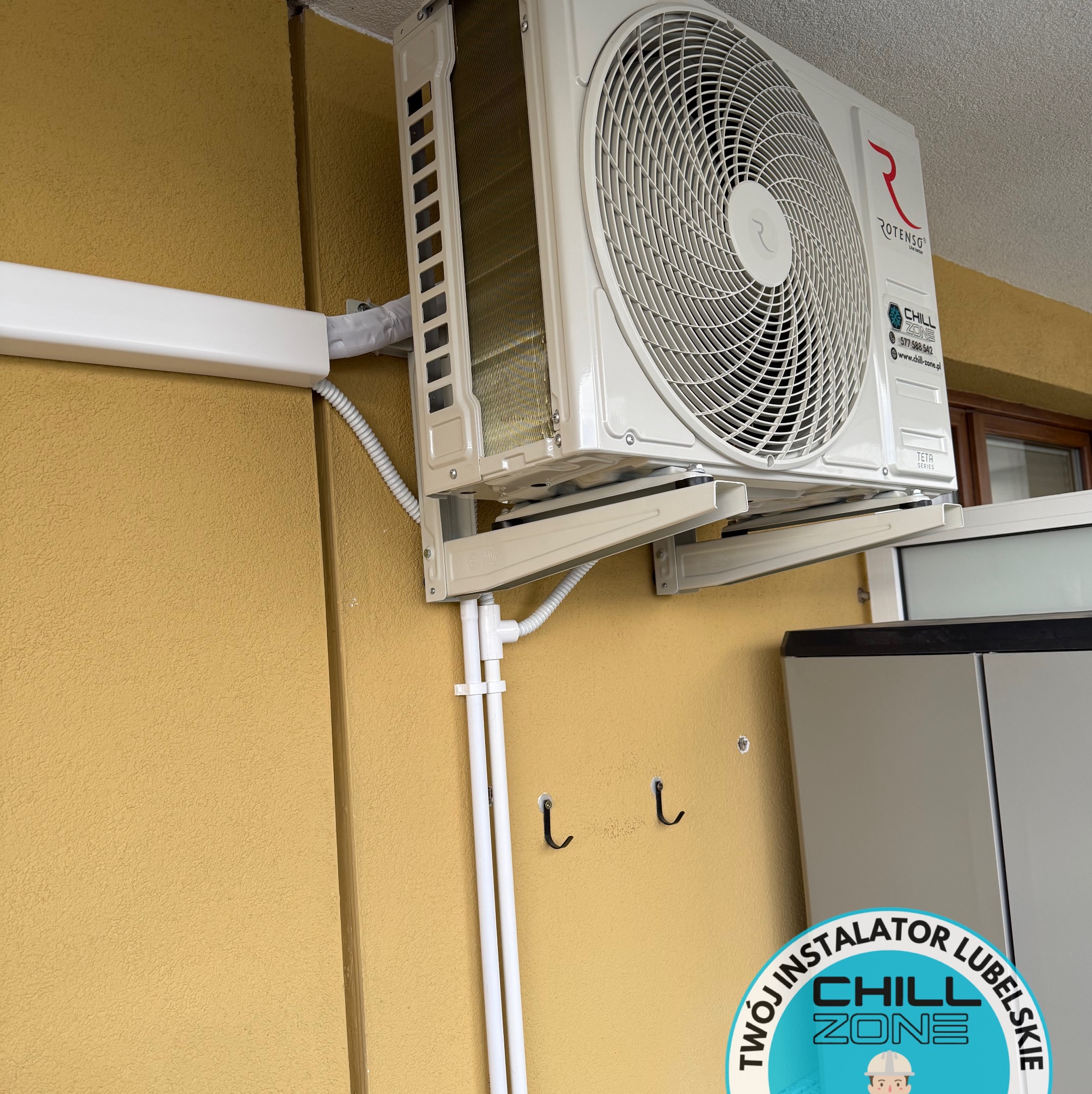 Zamontowana jednostka zewnętrzna klimatyzacji Rotenso na żółtej ścianie budynku, z widocznymi elementami instalacji i logiem firmy instalacyjnej Chill Zone Lubelskie.