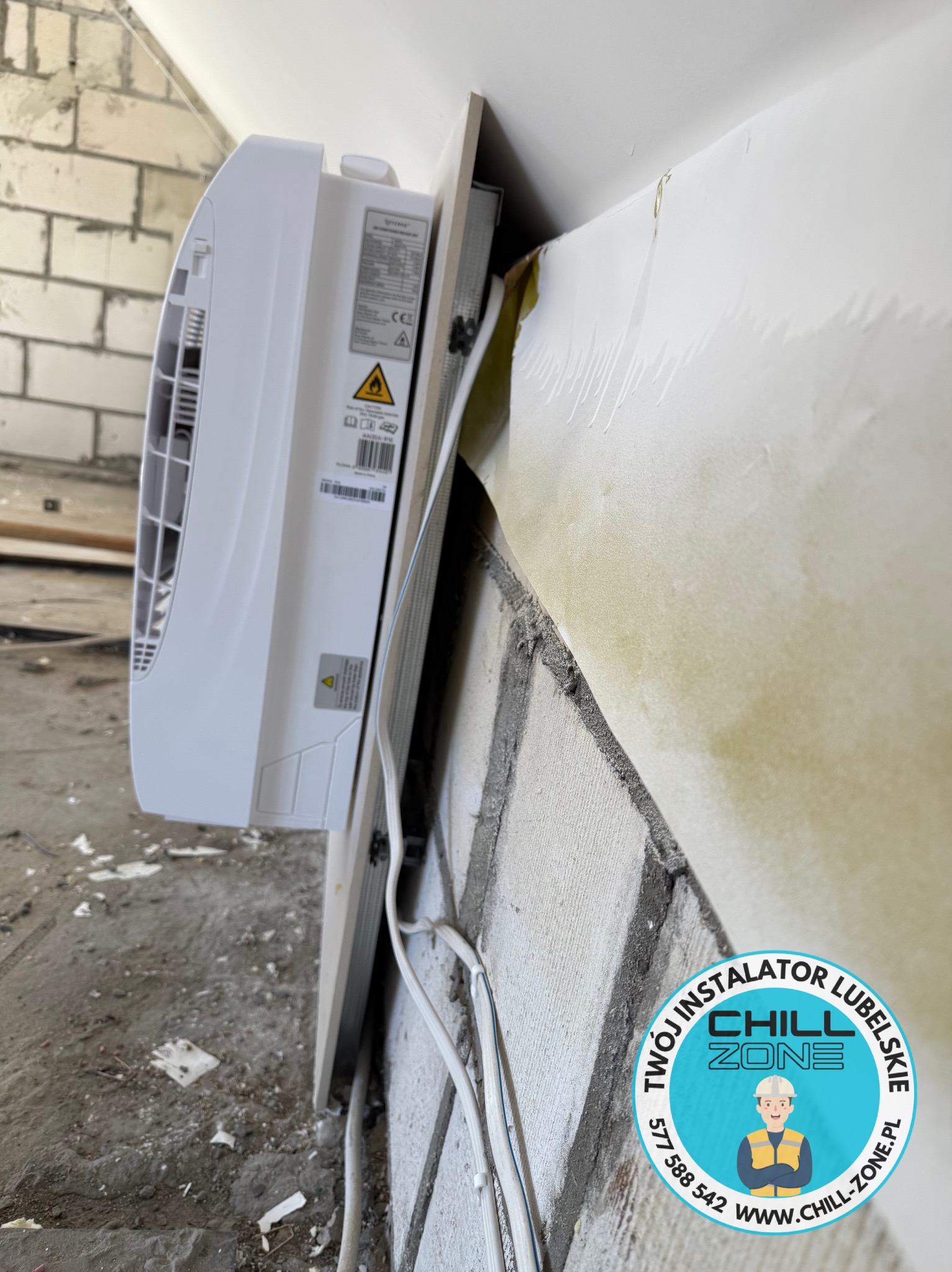 Boczny widok klimatyzatora na ścianie z cegły, instalacja w trakcie, widoczne przewody i logo firmy Chill Zone na ścianie.