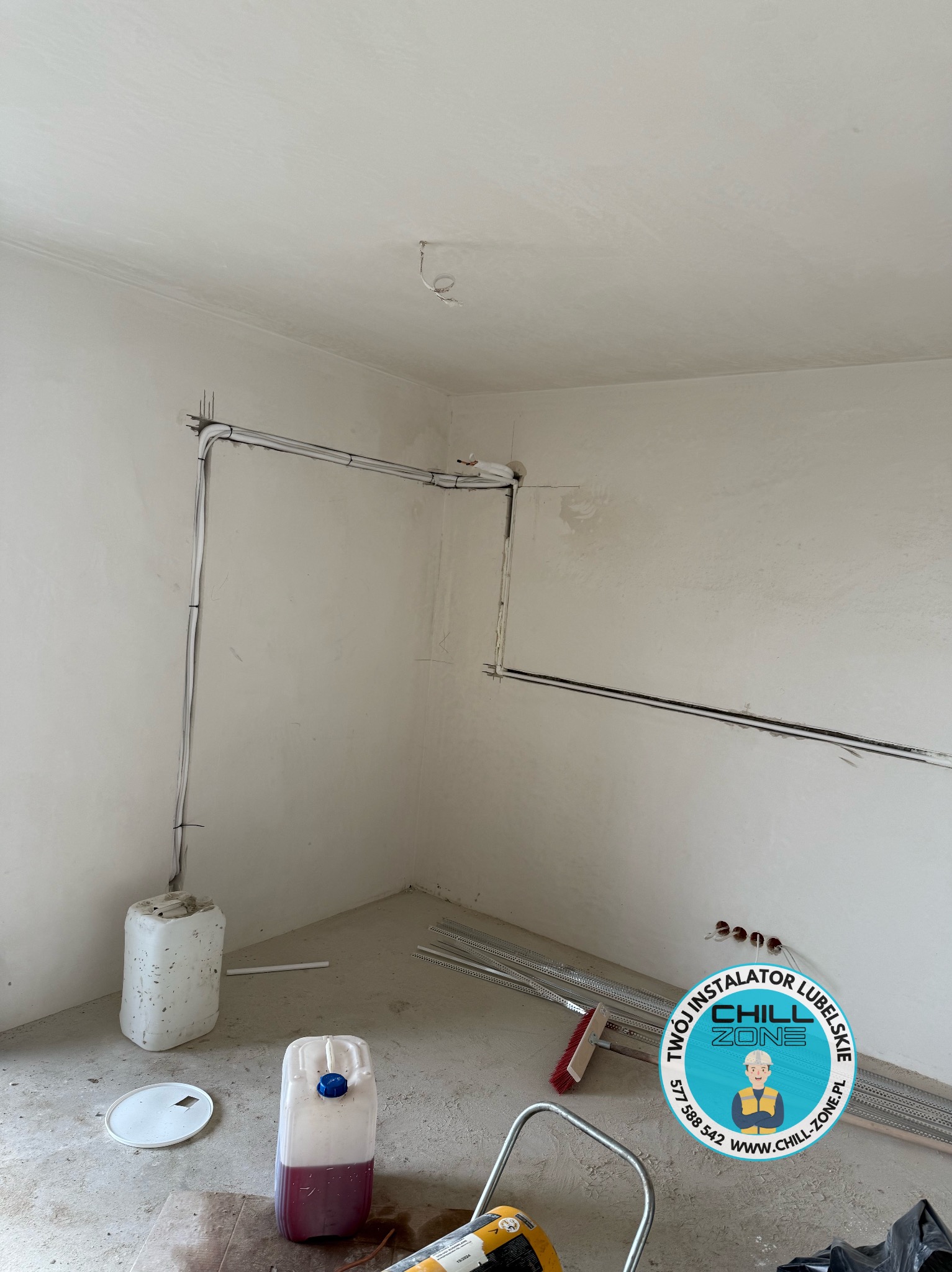 Wnętrze w trakcie montażu instalacji: rury prowadzone wzdłuż ścian, widoczne materiały budowlane i narzędzia. Ściany w surowym stanie, przygotowane do dalszych prac wykończeniowych.