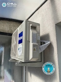 Zamontowany klimatyzator Haier na szarej ścianie, widoczny z boku, z naklejką informacyjną i logo firmy instalacyjnej. Częściowo widoczne elementy konstrukcyjne.