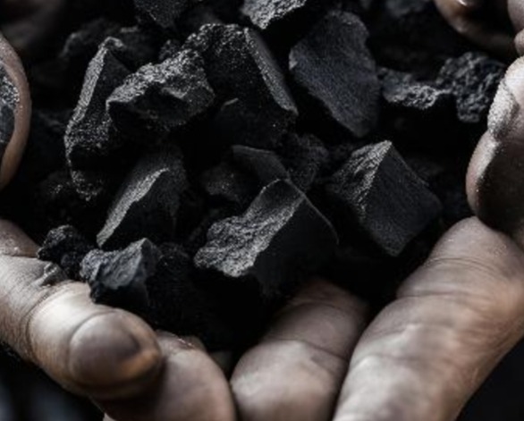 Dłonie robotnika trzymają bryły węgla kamiennego, widoczne ślady pyłu na skórze, ostre światło podkreśla teksturę materiału.