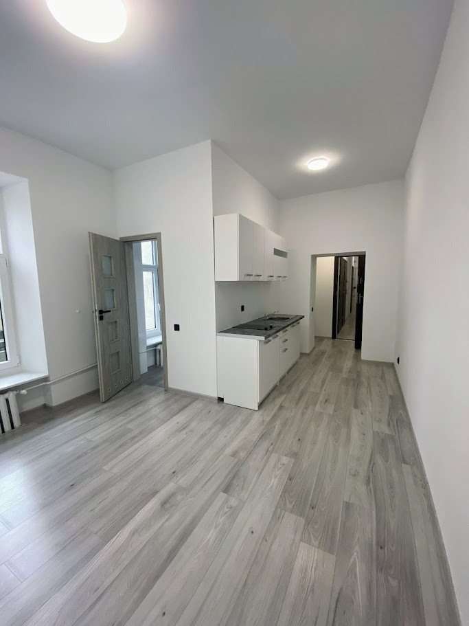 Jasne panele podłogowe w nowym, minimalistycznym mieszkaniu z białą kuchnią i drzwiami wewnętrznymi w odcieniach szarości.