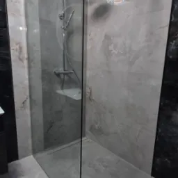 Nowoczesna kabina prysznicowa typu walk-in z deszczownicą, wykończona płytkami imitującymi marmur w odcieniach szarości i bieli, z widocznym odpływem liniowym.