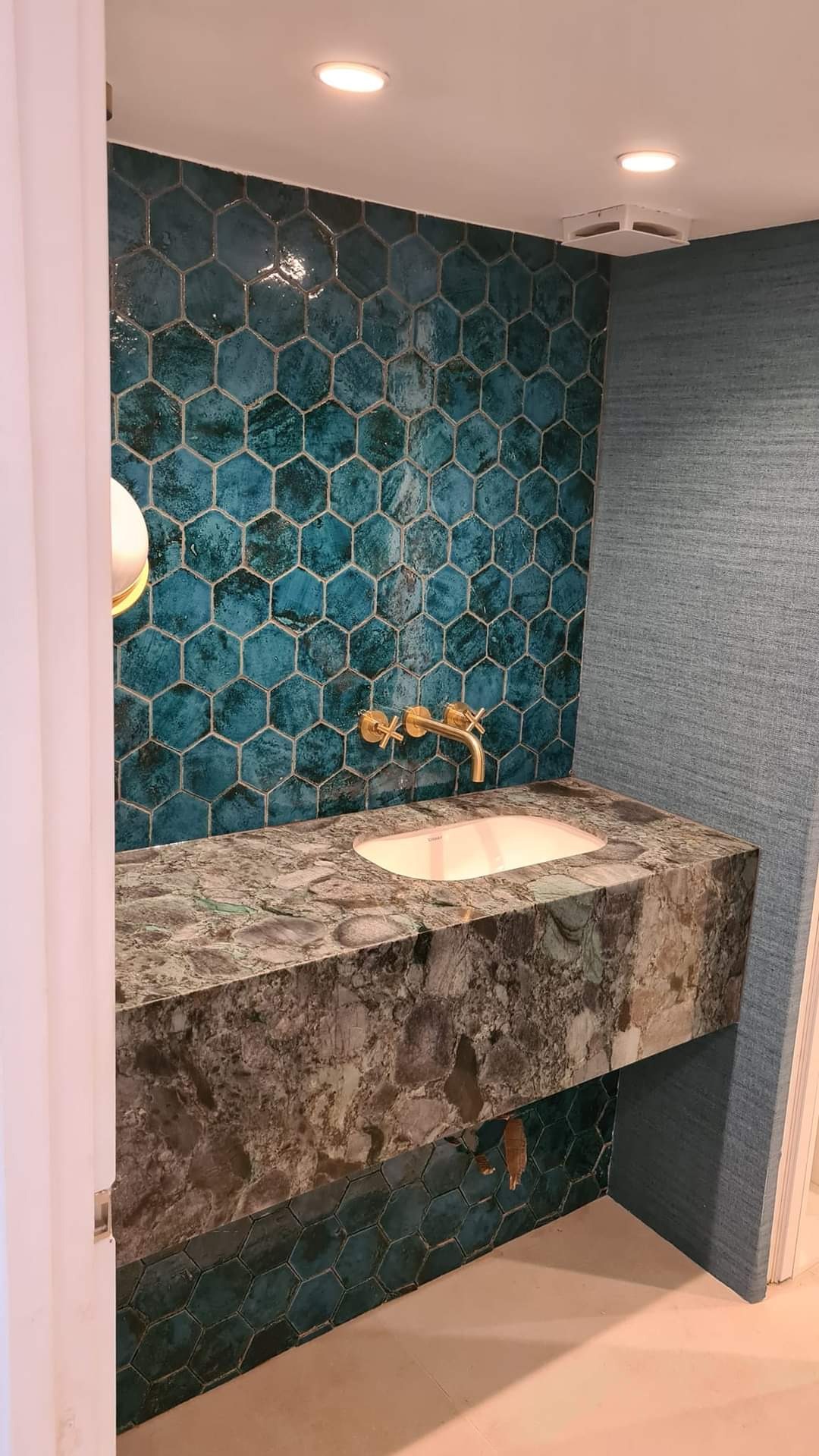 Łazienka z umywalką na blacie z zielonego agatu, ściana wyłożona turkusowymi heksagonalnymi płytkami, bateria umywalkowa w kolorze złotym