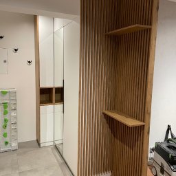 Rafał kloch - Wnętrze z szafą wnękową z białymi frontami i drewnianą ścianką działową z półkami, widoczny odkurzacz przemysłowy.