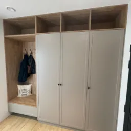 Zabudowa przedpokoju z szafą z szarymi frontami, otwartą wnęką z wieszakami i półką, oraz górnymi półkami z jasnego drewna.