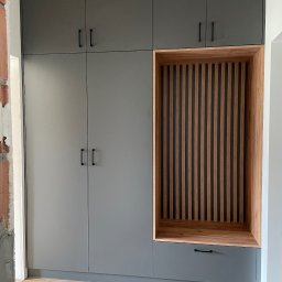 Rafał kloch - Szara szafa wnękowa z drewnianą wnęką z pionowymi listwami i szufladą, widoczne niedokończone wykończenie ściany.