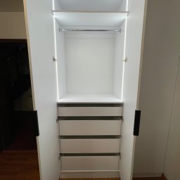 Rafał kloch - Wnętrze otwartej, białej szafy wnękowej z trzema szufladami, półką i drążkiem na ubrania, oświetlonej listwami LED, zrealizowanej w Tarnowie.
