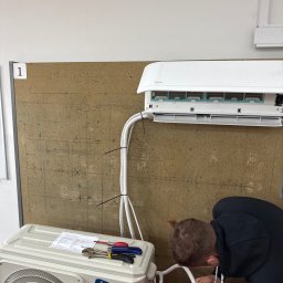 ZAKĄTEK SPÓŁKA Z OGRANICZONĄ ODPOWIEDZIALNOŚCIĄ - Instalacja klimatyzacji Airwell: monterzy podłączają przewody, na agregacie leżą narzędzia i specyfikacja techniczna.