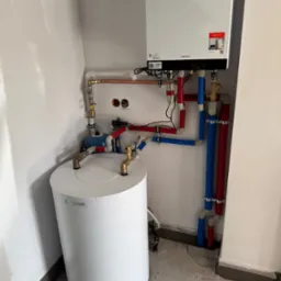 Nowoczesny piec gazowy Viessmann z podłączonym zasobnikiem ciepłej wody i instalacją z rur w kolorach czerwonym i niebieskim w narożniku pomieszczenia.