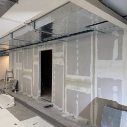 Oskar Fundalski - Wnętrze biura w trakcie remontu: ściany z płyt karton-gips, widoczne profile sufitowe i drabina. Surowy stan wykończenia, przygotowanie do dalszych prac.