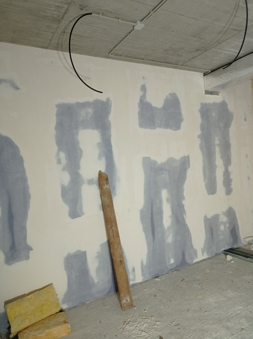 Przygotowanie ściany pod malowanie: szpachlowanie ubytków. Widoczne kable pod sufitem, deska oparta o ścianę i fragment wełny mineralnej. Surowy stan wnętrza.