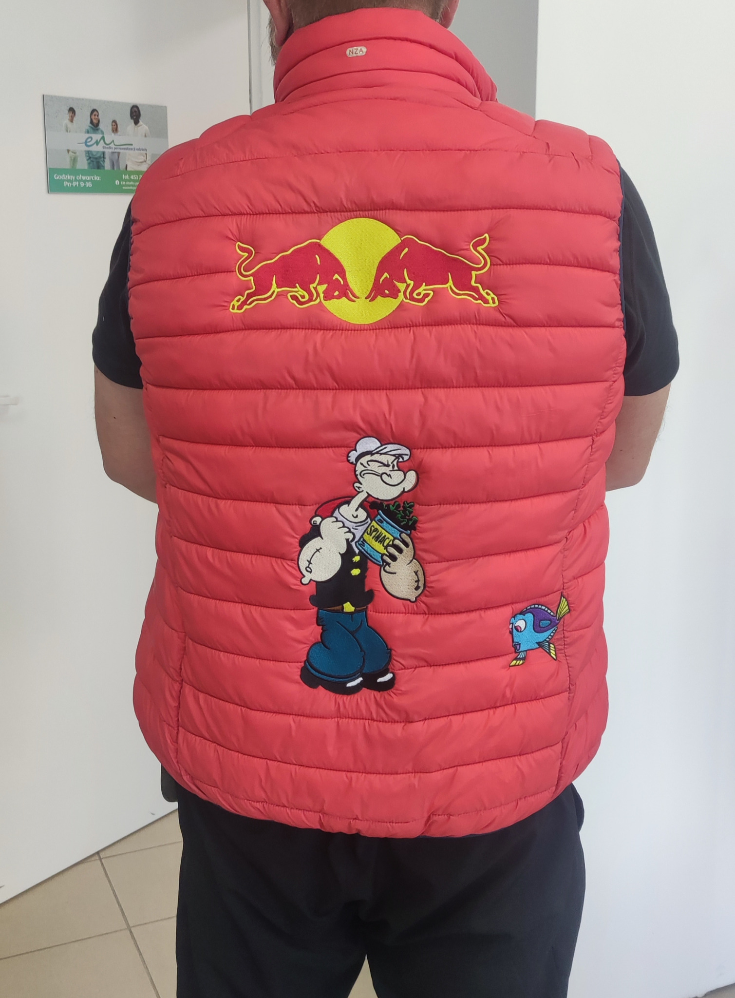 Czerwona, pikowana kamizelka z haftowanymi aplikacjami: logo Red Bull, Popeye jedzący szpinak i rybka Dory, widok z tyłu na mężczyźnie.
