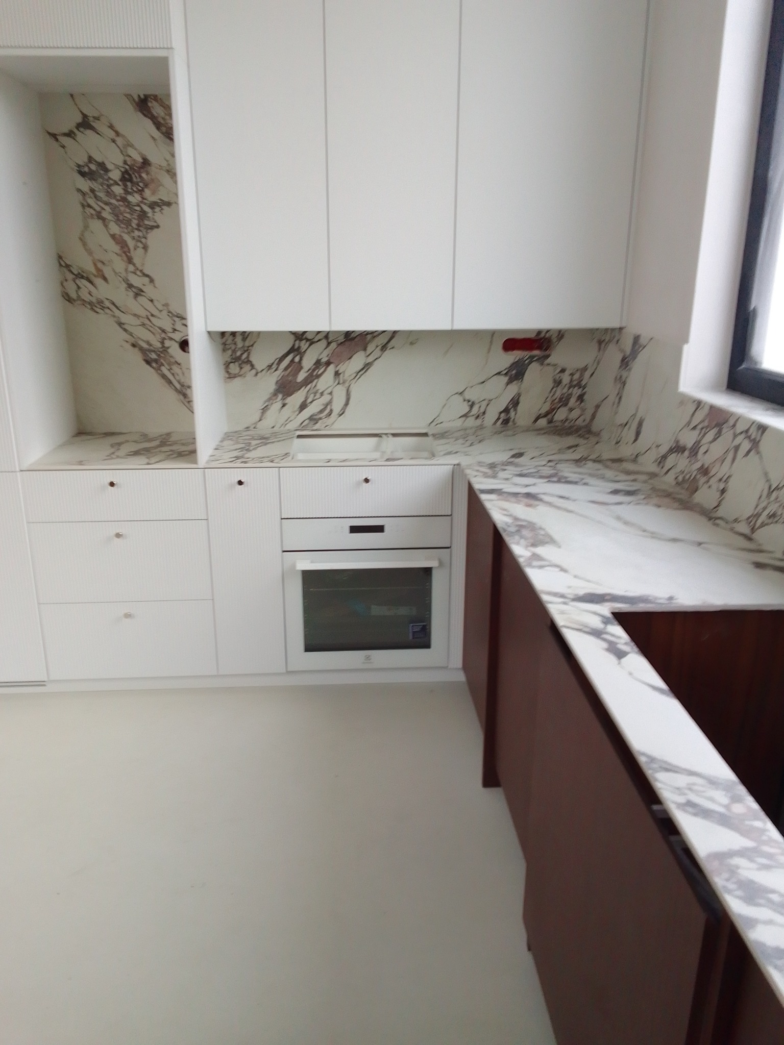 Nowoczesna kuchnia z białymi szafkami i blatem z marmuru Calacatta Viola, brązowe szafki dolne, widoczny zlew i piekarnik.