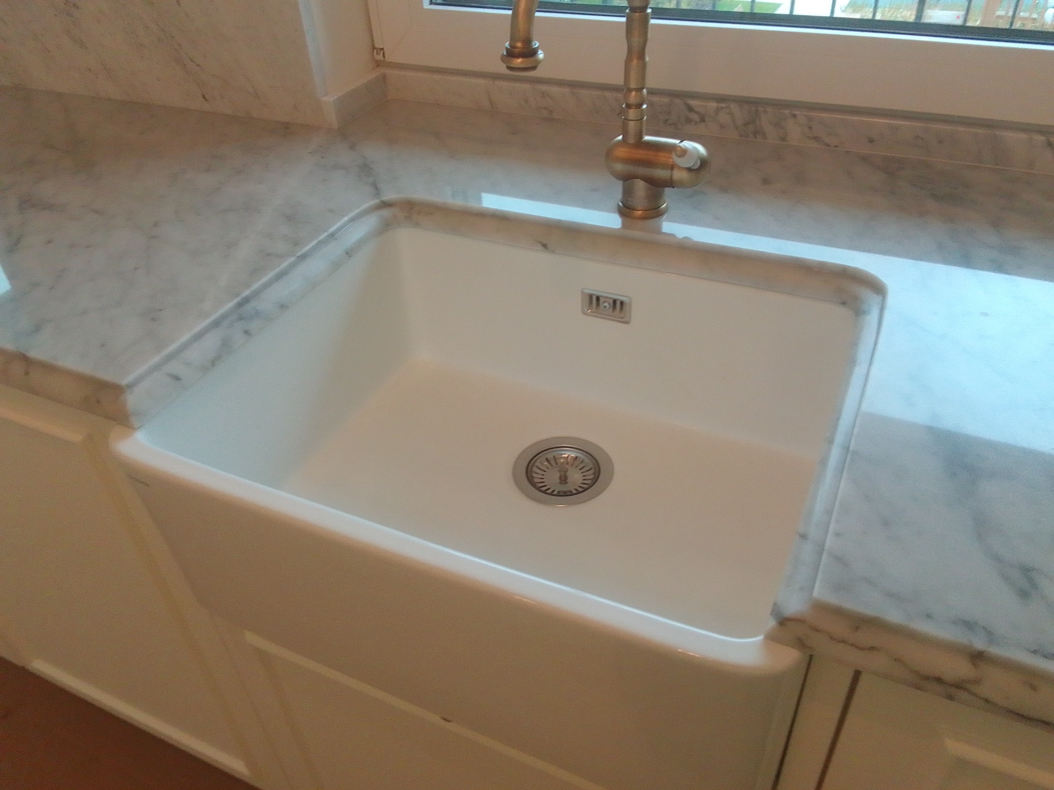 Biały, ceramiczny zlew gospodarczy wbudowany w marmurowy blat, bateria w kolorze starego złota, widok z góry.