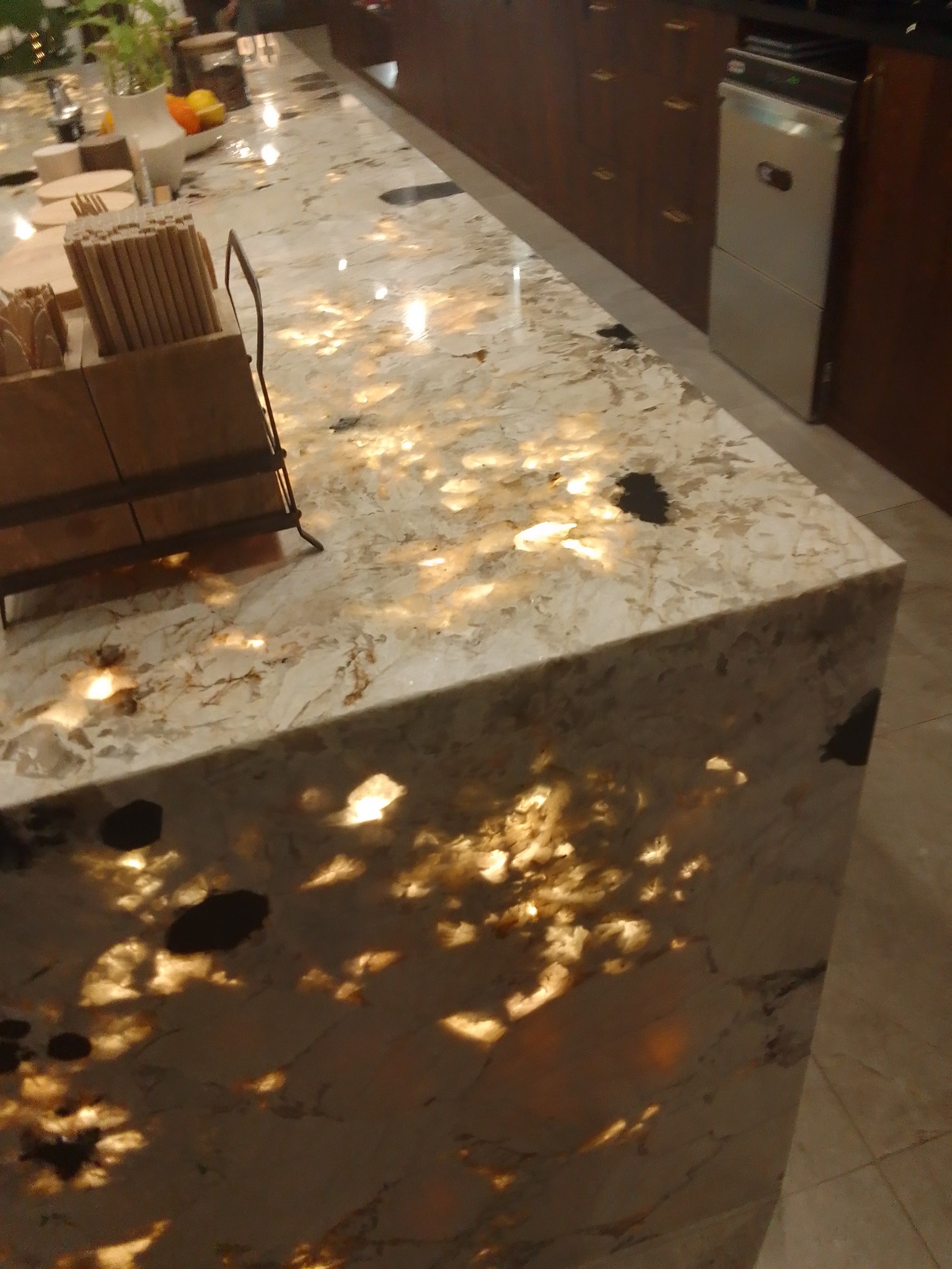 Błyszczący blat z kamienia naturalnego w kuchni, z widocznymi inkluzjami i unikalnym wzorem, oświetlony od spodu, z elementami wyposażenia na wierzchu.