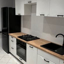 Marcin Florek Cactus Ink - Nowoczesna kuchnia w bieli i czerni z drewnianym blatem, widoczne folie ochronne na frontach szafek sugerujące świeży montaż.