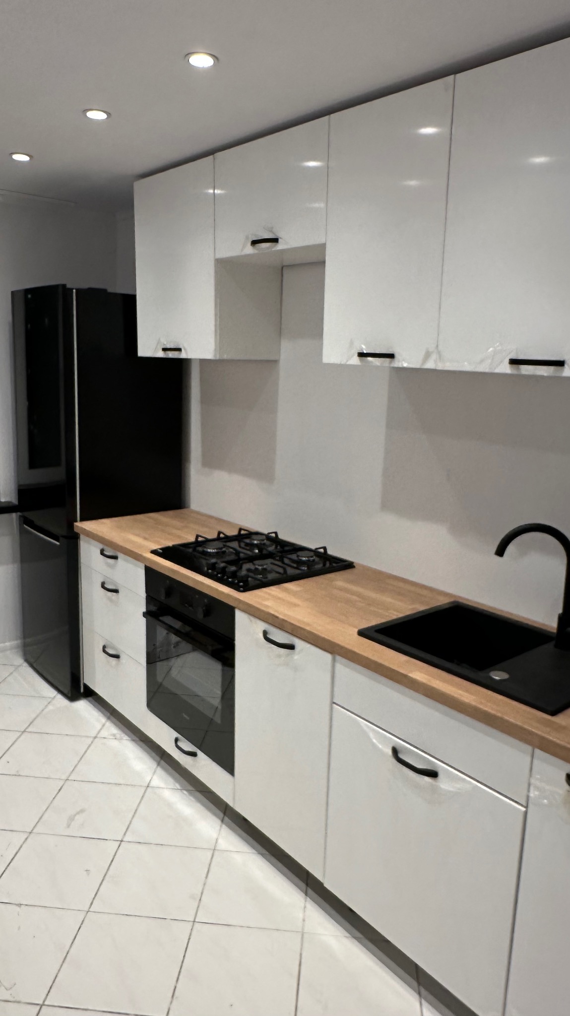 Nowoczesna kuchnia w bieli i czerni z drewnianym blatem, widoczne folie ochronne na frontach szafek sugerujące świeży montaż.
