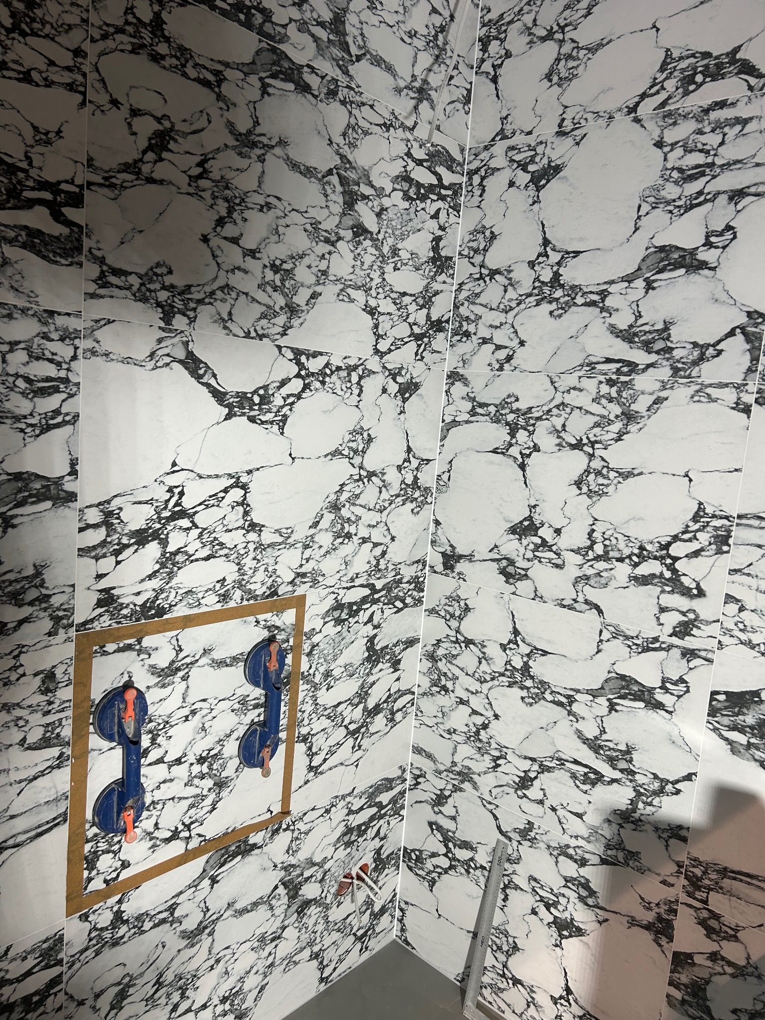 Montaż płytek imitujących marmur na ścianie we Wrocławiu, widoczne przyssawki do płytek i fragment instalacji.