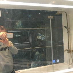 DR.HOUSE - Nowoczesna łazienka z kabiną prysznicową, wykończona płytkami w odcieniach zieleni i złota. Widoczne elementy armatury i oświetlenie.