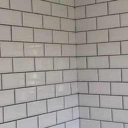 DR.HOUSE - Ściana wyłożona białymi, prostokątnymi płytkami z ciemną fugą, widok z narożnika. Minimalistyczny design, charakterystyczne wykończenie ściany w łazience lub kuchni.