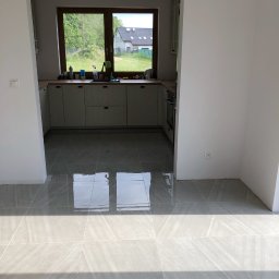 DR.HOUSE - Jasna kuchnia z szarymi płytkami podłogowymi, widokiem na zieleń przez okno. Świeżo wyremontowane wnętrze, minimalistyczny styl.