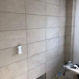 DR.HOUSE - Ściana z beżowych płytek w łazience w trakcie remontu. Widoczna puszka elektryczna i drabina z narzędziami. Fragment podłogi bez płytek.