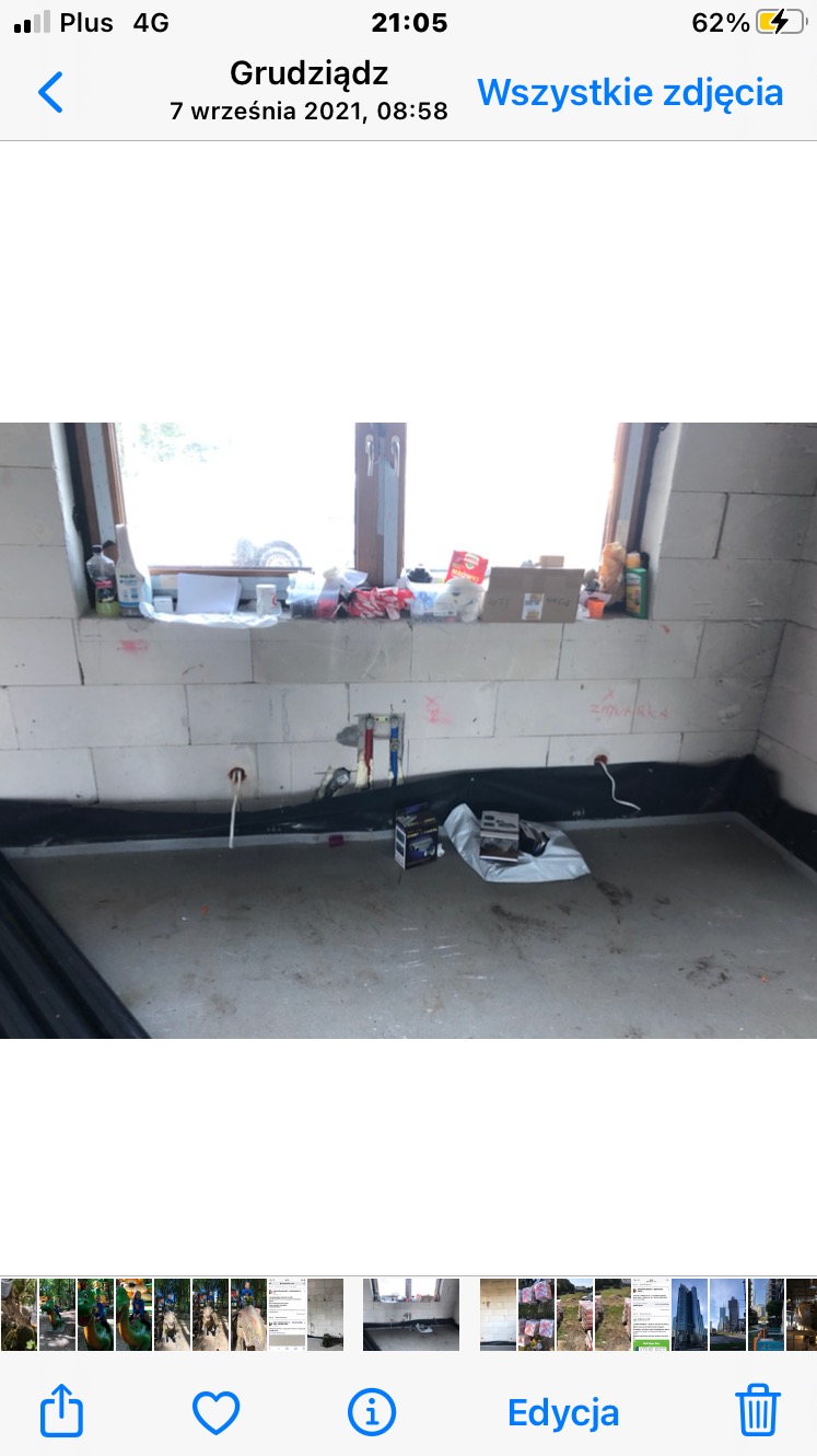 Surowa łazienka w trakcie remontu: białe bloczki, okno z parapetem zastawionym przedmiotami, instalacja wodna w ścianie, czarna izolacja przeciwwilgociowa.