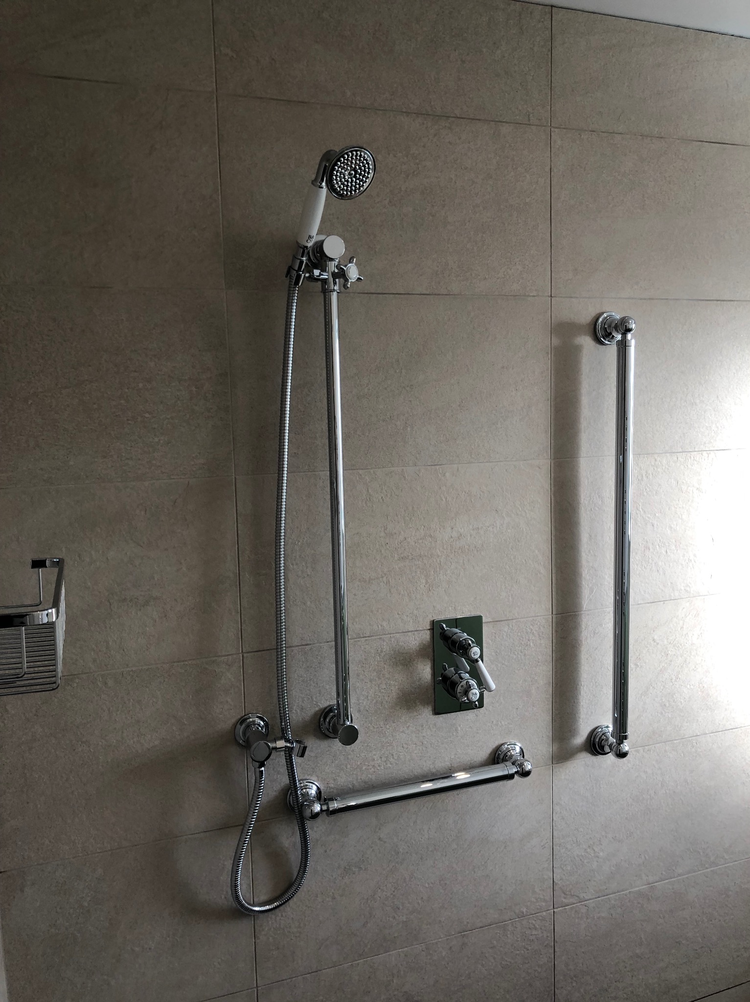 Wykończona łazienka z beżowymi płytkami. Zamontowany chromowany zestaw natryskowy z deszczownicą, bateria podtynkowa i uchwyt dla niepełnosprawnych. Nowoczesny design.