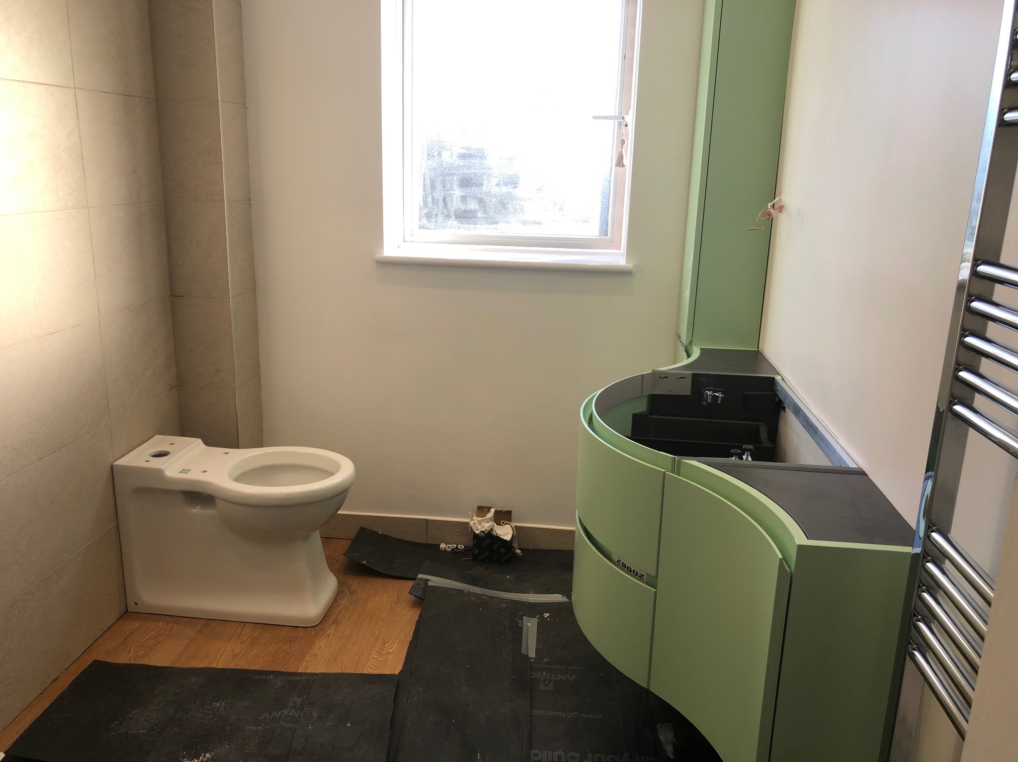 Łazienka w trakcie prac: podwieszana toaleta bez spłuczki obok zabudowy umywalkowej w odcieniach zieleni, na podłodze folia zabezpieczająca.