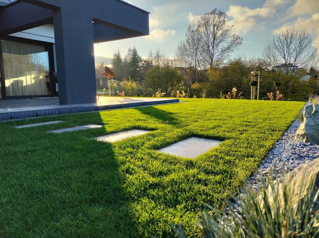 Nowoczesny ogród z równo przystrzyżonym trawnikiem, kwadratowymi płytami chodnikowymi w trawie i ozdobnym kamiennym obrzeżem.