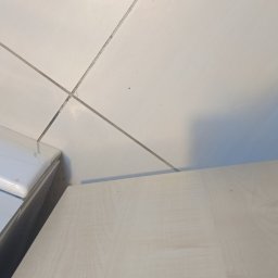 KZ Cleaning Services - Fragment podłogi z białych płytek w Bochni, widoczna dolna część szafki oraz but osoby stojącej obok.