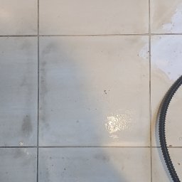 KZ Cleaning Services - Czyszczenie podłogi z płytek: widoczny fragment buta osoby czyszczącej, brudne i częściowo umyte płytki oraz wąż prawdopodobnie od odkurzacza parowego.