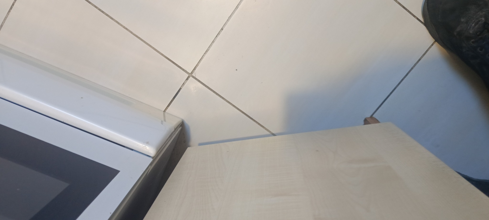 Fragment podłogi z białych płytek w Bochni, widoczna dolna część szafki oraz but osoby stojącej obok.