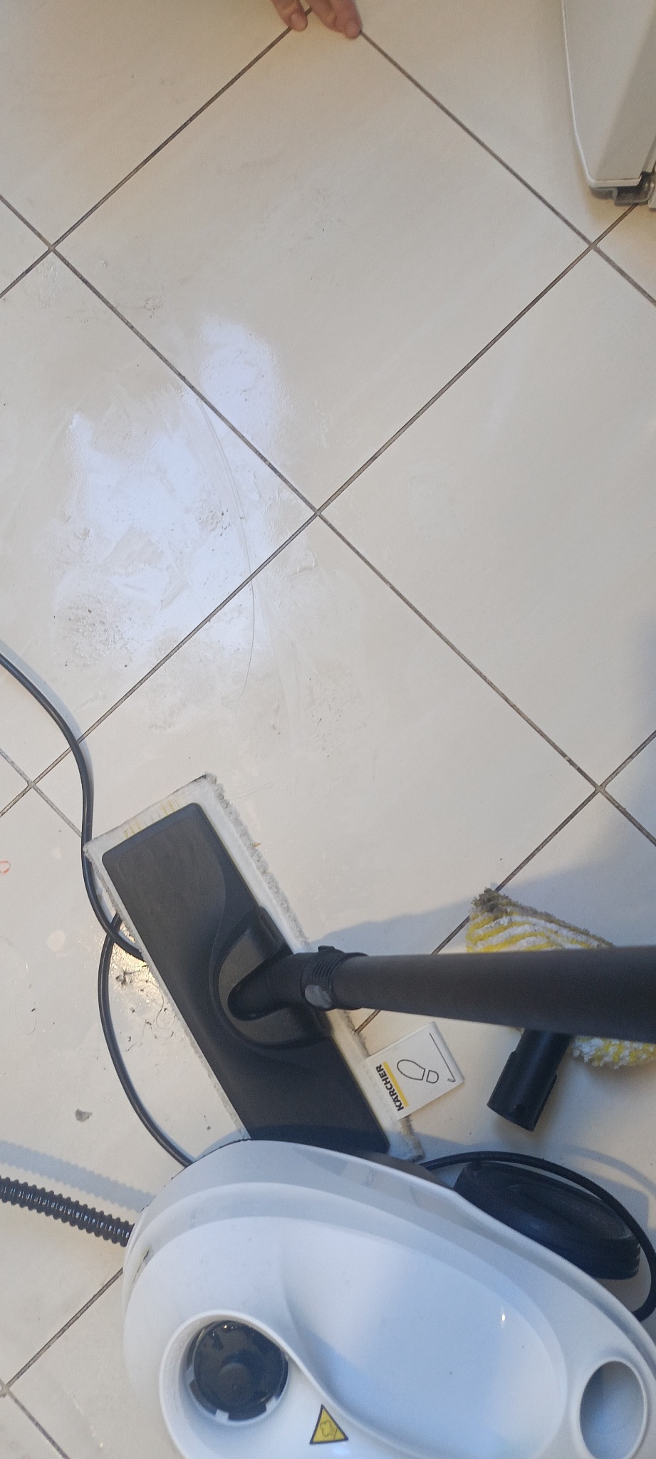 Parownica Kärcher z czarną dyszą i żółtą ściereczką do czyszczenia płytek podłogowych. Widoczne ślady użycia na białych płytkach.