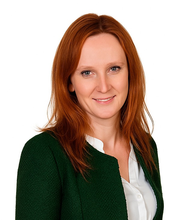 Portret uśmiechniętej kobiety z rudymi włosami w zielonej marynarce na białym tle. Profesjonalny wizerunek.