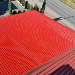 GREEN MASTER MYKHAILO BURDOVSKYI - Czerwony blaszany dach z widoczną fakturą, sfotografowany z góry, z fragmentem ulicy i samochodu w tle.