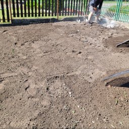 GREEN MASTER MYKHAILO BURDOVSKYI - Przygotowanie podłoża pod trawnik: wyrównywanie ziemi grabiami i usuwanie resztek gruzu, widoczny fragment ogrodzenia w tle.