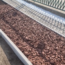 GREEN MASTER MYKHAILO BURDOVSKYI - Krawężnik oddzielający rabatę z kory drzewnej od białych kamyków przy metalowym ogrodzeniu.